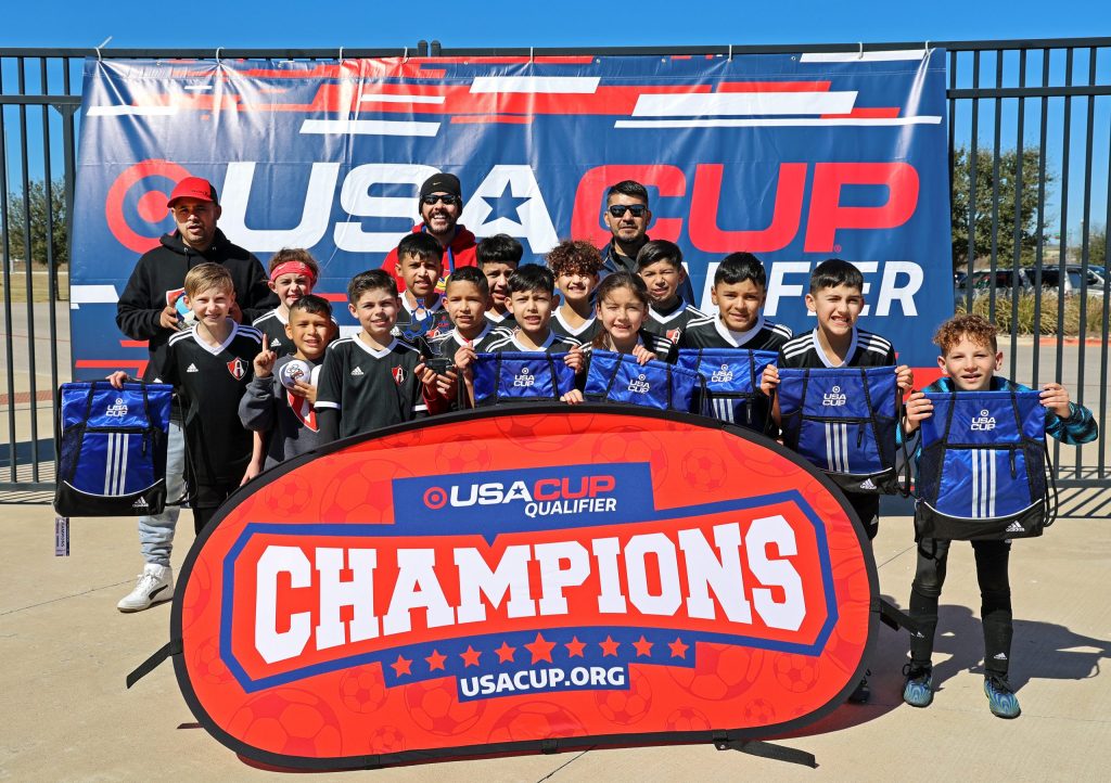 FC Atlas 11U boys holding up player bags in front of a champions sign.